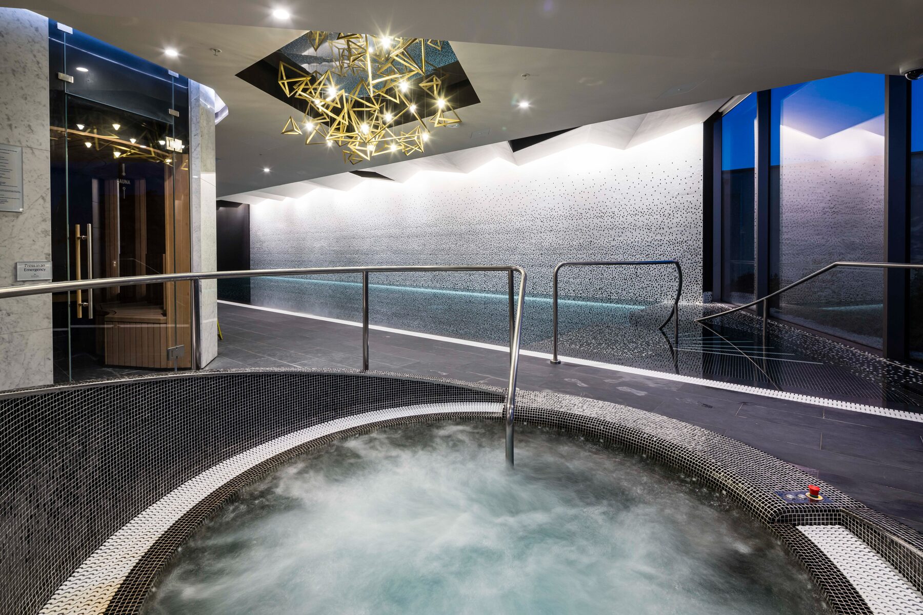 Vitality pool beneath a sculptural brass chandelier, sauna beyond